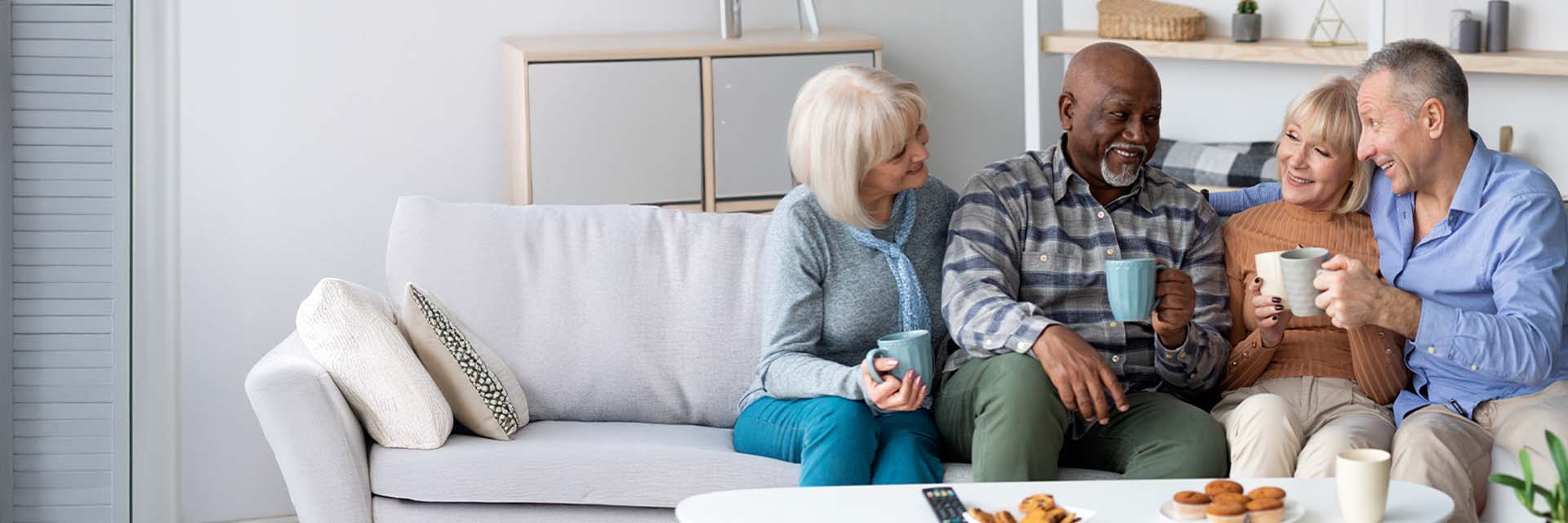 Senior living community group enjoying coffee together and chatting on a couch.