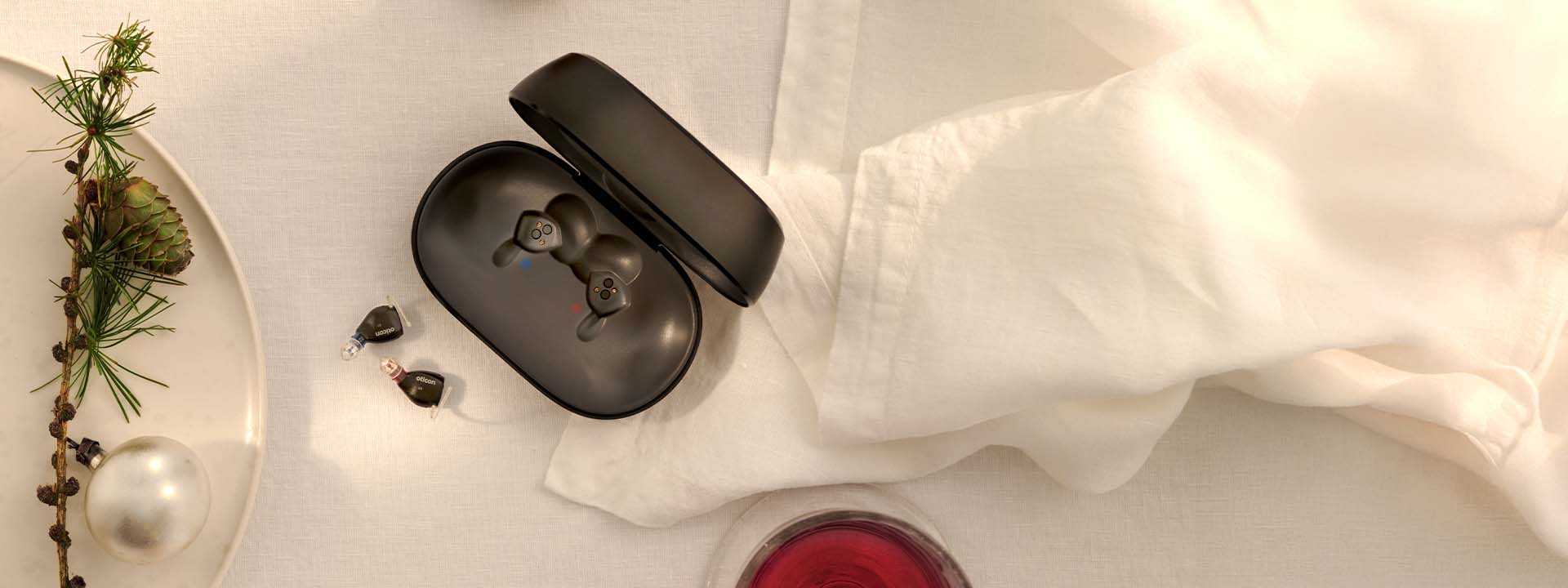 NEW Oticon Zeal™ hearing aids displayed with charger on a holiday-inspired table setting.