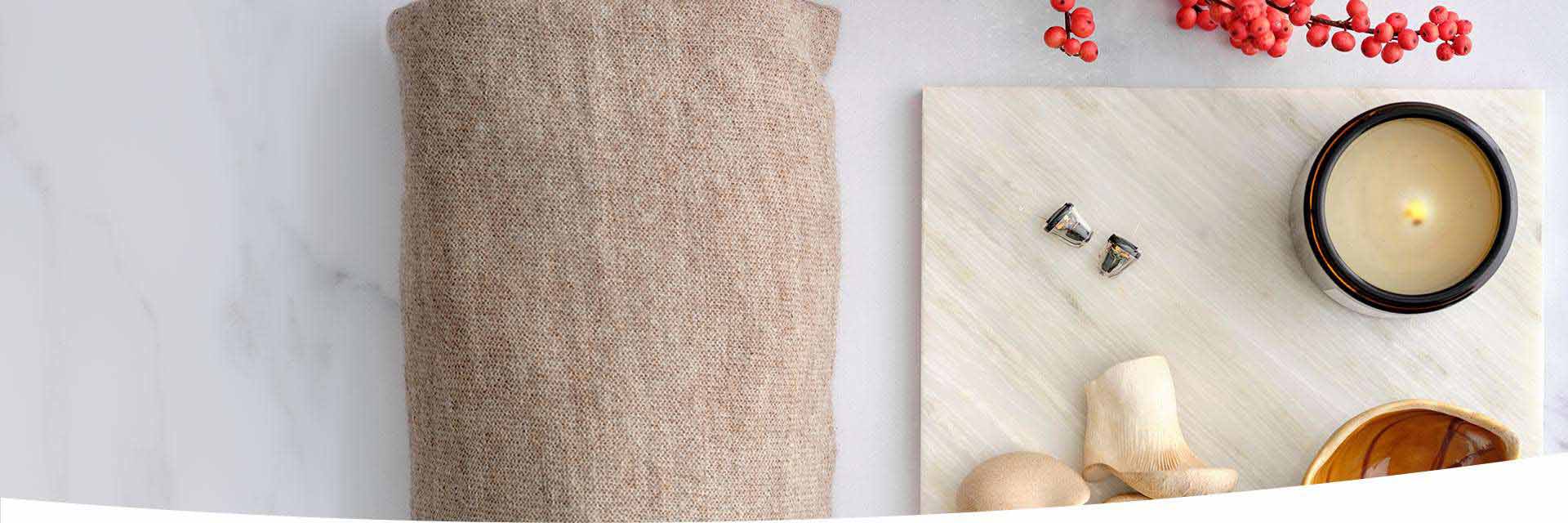 Oticon OWN SI™ hearing aids placed on a decorative surface alongside a candle, fabric, and small wooden elements.