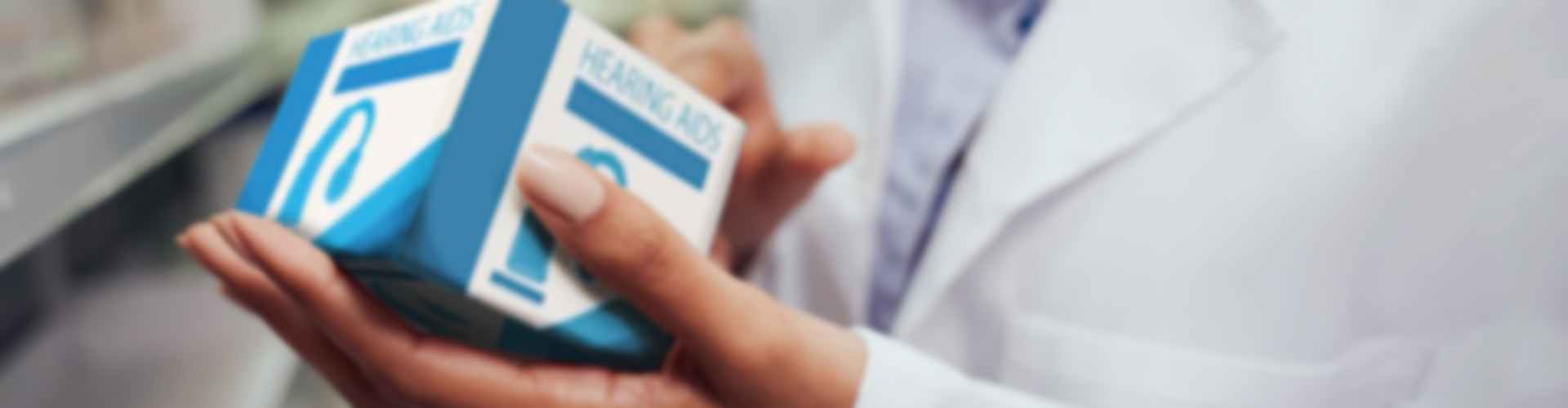 Pharmacist presenting a box of over-the-counter hearing aids in a pharmacy environment.