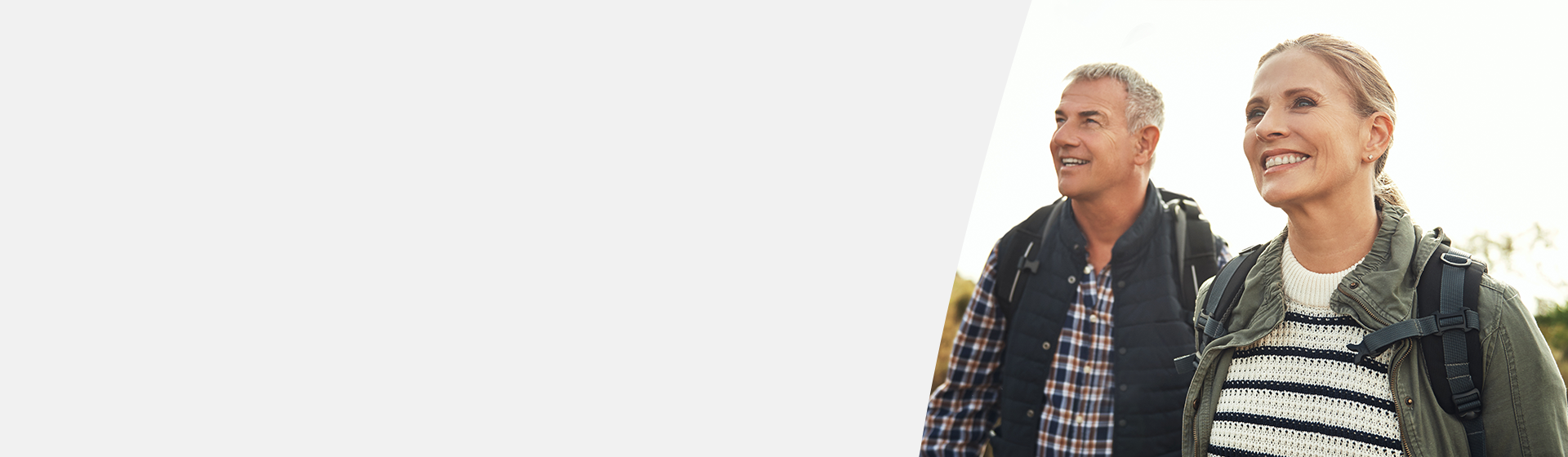 Older couple enjoying an outdoor hike while wearing casual jackets and backpacks.