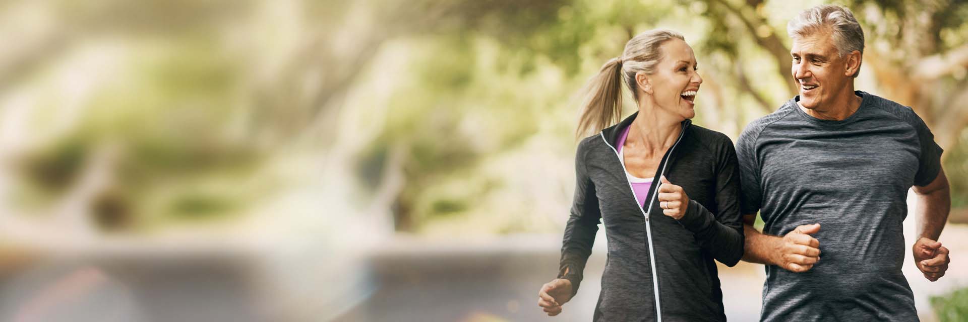 Couple jogging outdoors, smiling and engaging in conversation amidst a blurred natural background.