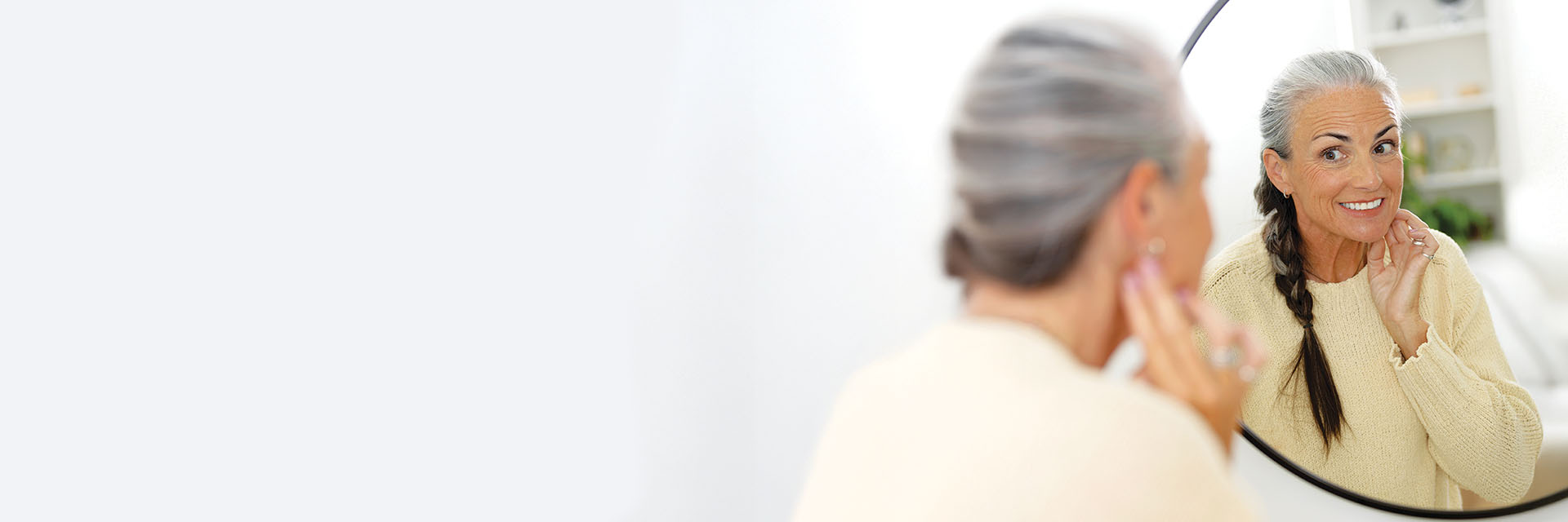 Smiling woman wearing hearing aid while checking her reflection in a mirror.