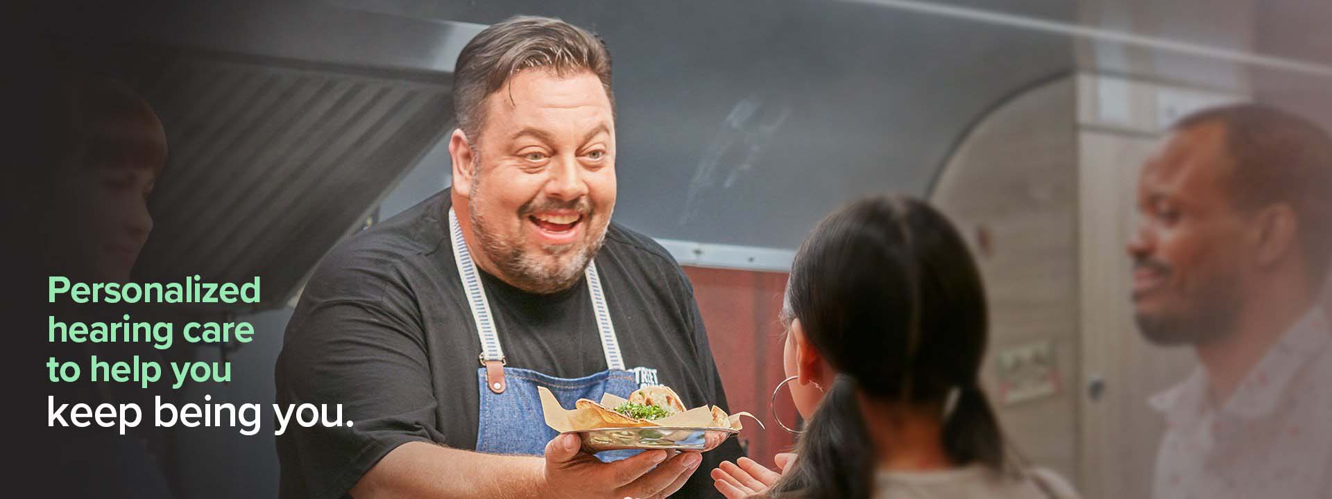 Personalized hearing care to help you keep being you. (Nico smiling as he serves food from his food truck).)