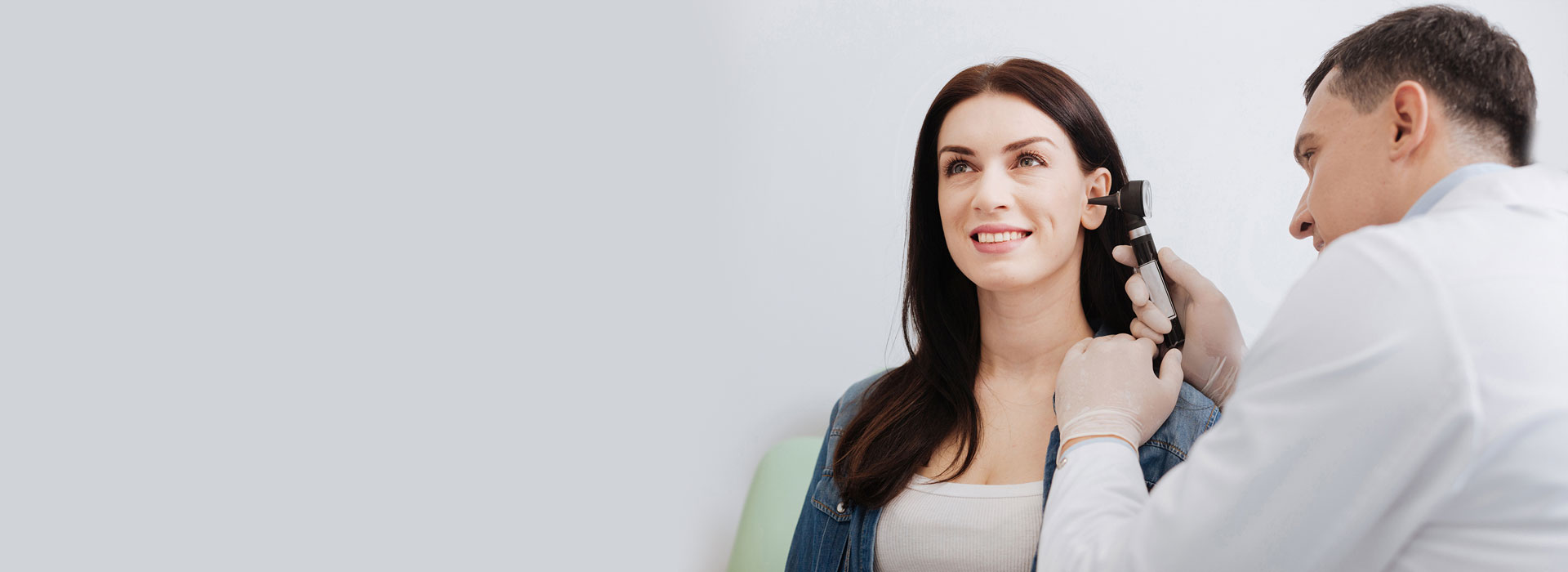 Audiologist conducting an ear examination using an otoscope on a smiling patient.
