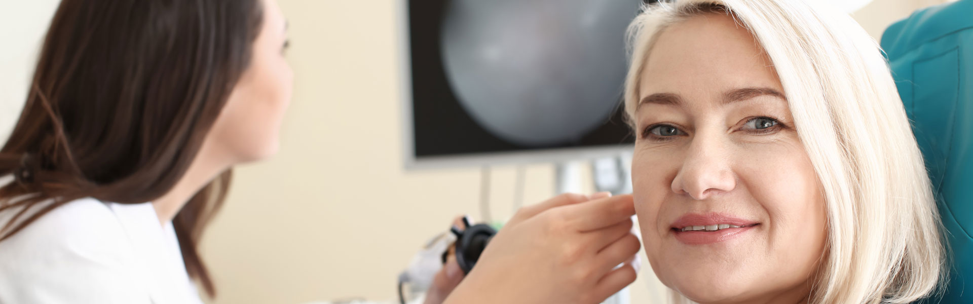 Woman undergoing a hearing care check with audiology equipment displayed in the background.