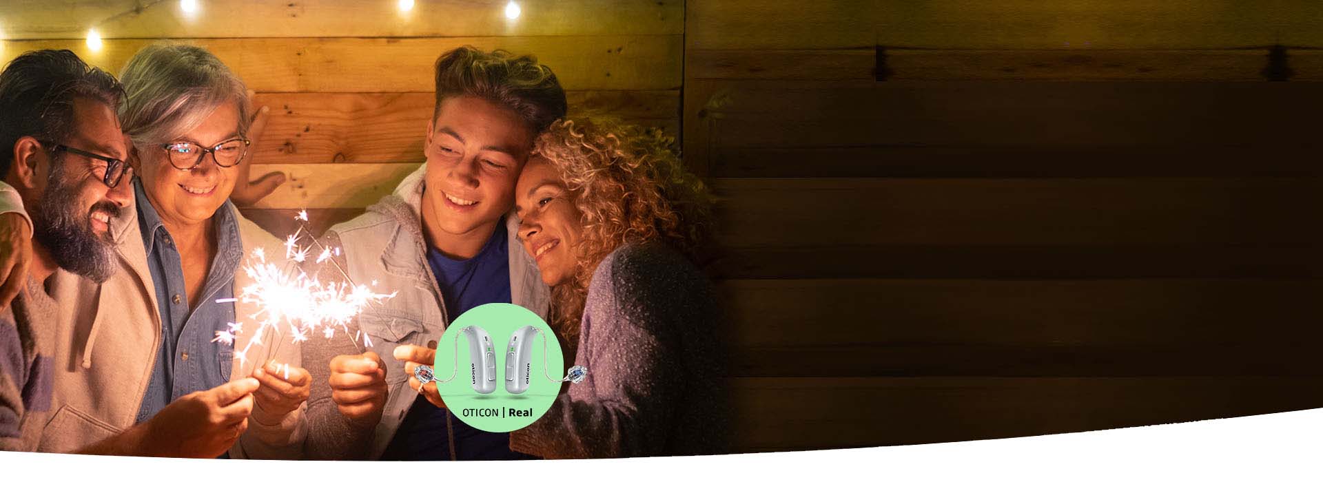 Hearing aids placed next to a small flower with people holding sparklers in the background.