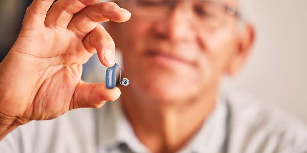 Hand holding a small blue hearing aid, featured in a close-up with a blurred background.