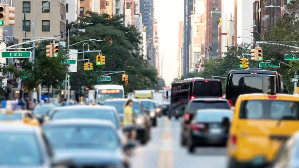 Busy New York City street with cars, traffic lights, and urban buildings in the background.