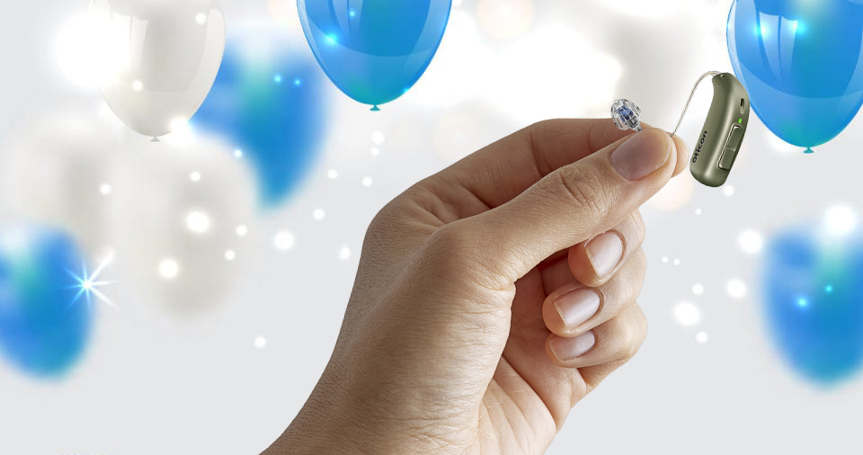 A hand holds a small, green hearing aid device labeled 