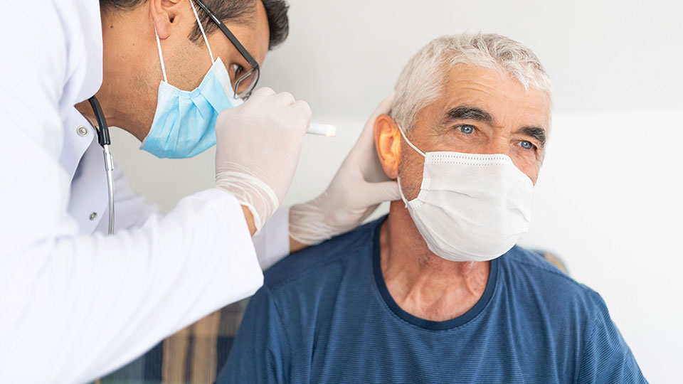 Audiologist conducting an ear examination on a senior patient wearing a face mask.