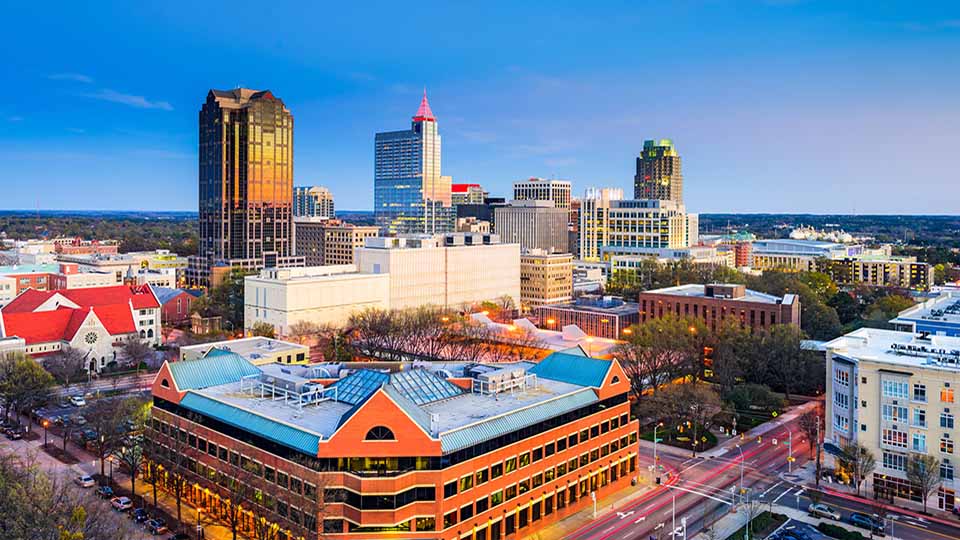 Downtown Raleigh, NC skyline at sunset with modern buildings and tree-lined streets.