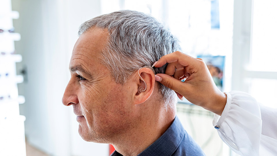 Man being fitted with a behind-the-ear hearing aid by a hearing care professional.
