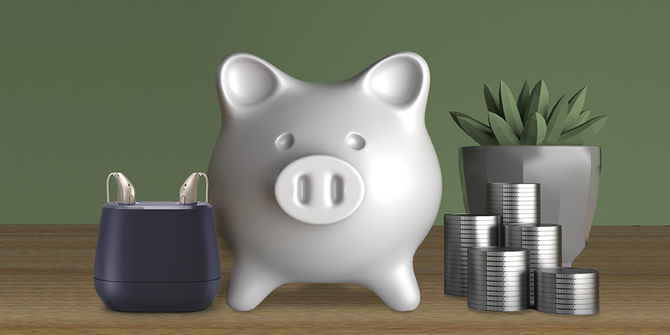 Rechargeable hearing aids in a charging case positioned alongside a white piggy bank, stacks of coins, and a potted plant on a wooden surface.