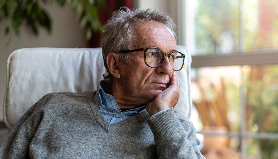 melancholy elderly man sitting near a window and gazing thoughtfully outdoors