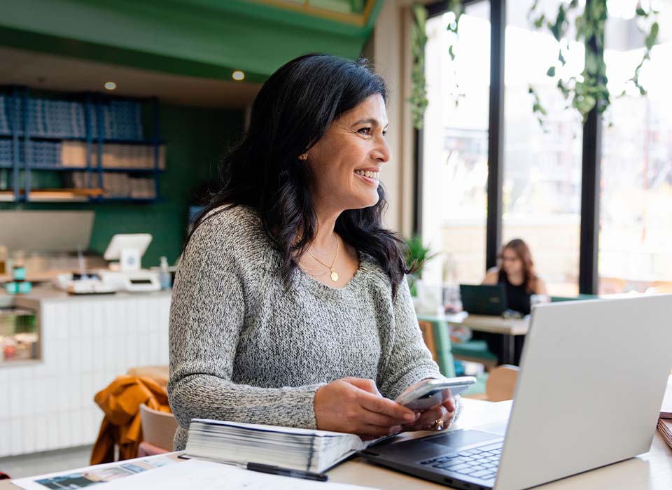 Woman in coffee show working on laptop and smiling