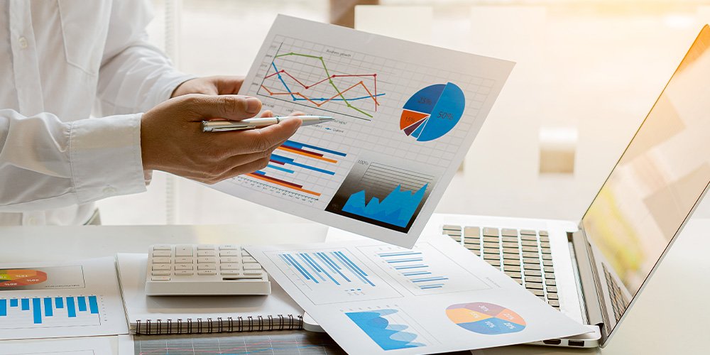 Analyzing business charts and graphs on paper near a laptop