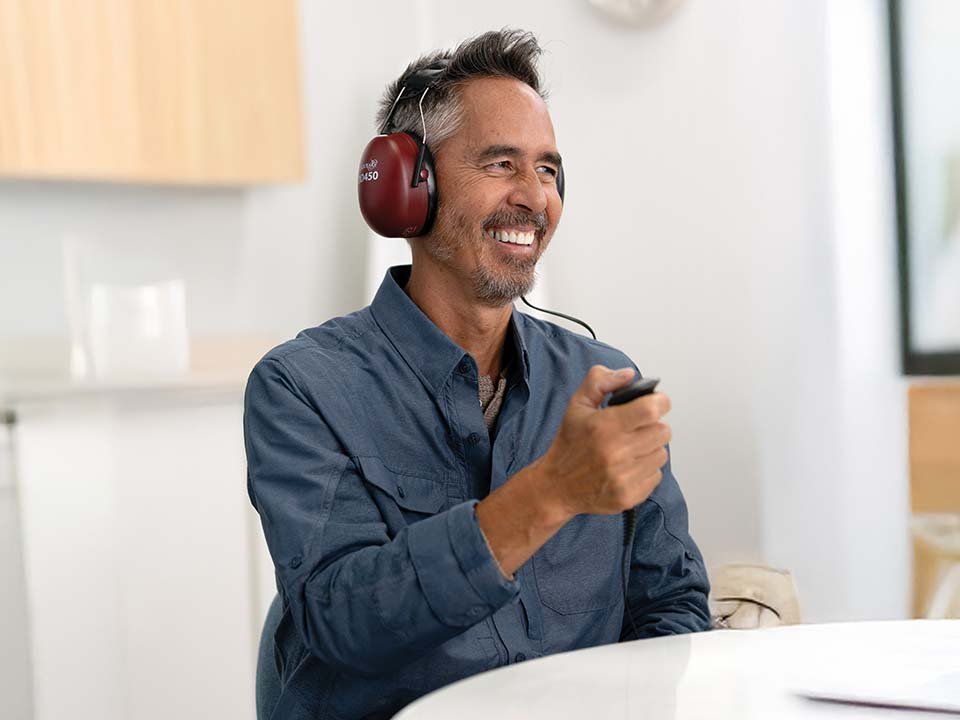 Man smiling as he takes online hearing test wearing headphones