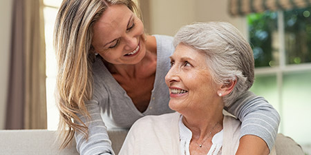 Older woman wearing a hearing aid smiling and talking with a younger woman indoors.
