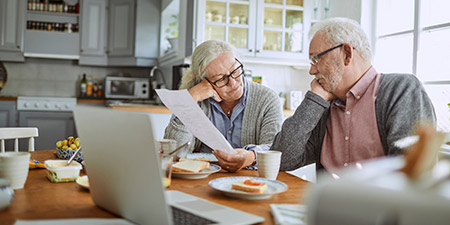 Senior couple reviewing paperwork together at the breakfast table in a bright kitchen.