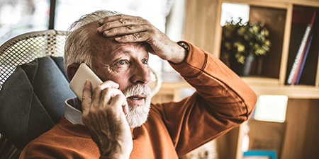 Senior man holding his head while talking on a smartphone at home.
