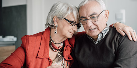 Older couple sitting close together, smiling and embracing, showcasing warmth and connection.