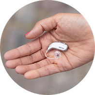 Hand holding a small, modern hearing aid with a transparent earpiece.