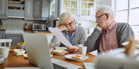 Senior couple reviewing paperwork together at the breakfast table in a bright kitchen.