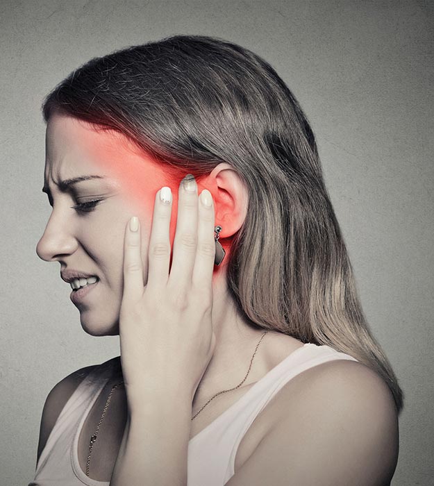 Woman experiencing ear pain, holding her ear with visible redness around the area.