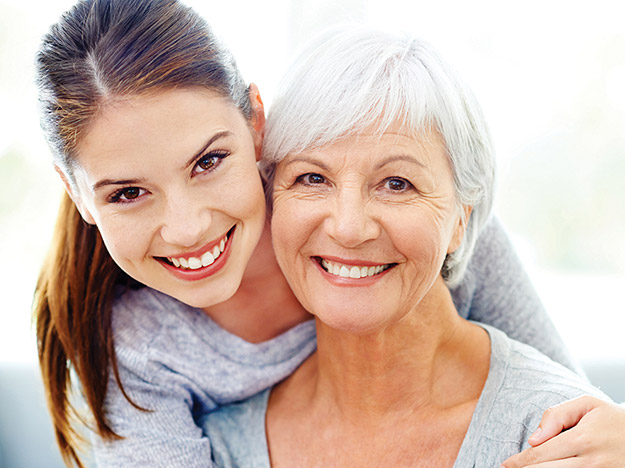 Two women smiling, one with gray hair and the other with brown hair, embracing in a warm, cheerful moment.