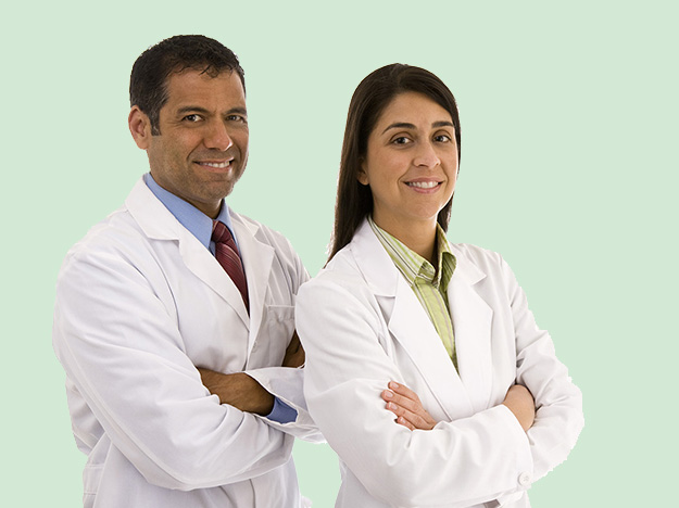 Doctors smiling confidently in white lab coats with arms crossed, standing against a light green background.
