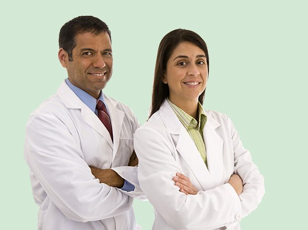 Two doctors stand smiling with arms crossed, wearing white lab coats, against a light green background.