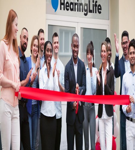 Grand opening celebration at a new HearingLife center with a ribbon-cutting ceremony surrounded by a group of people.