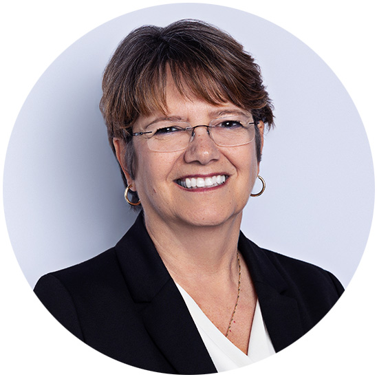 A woman smiles confidently with her arms crossed, wearing a black shirt and eyeglasses, set against a plain white circular background.