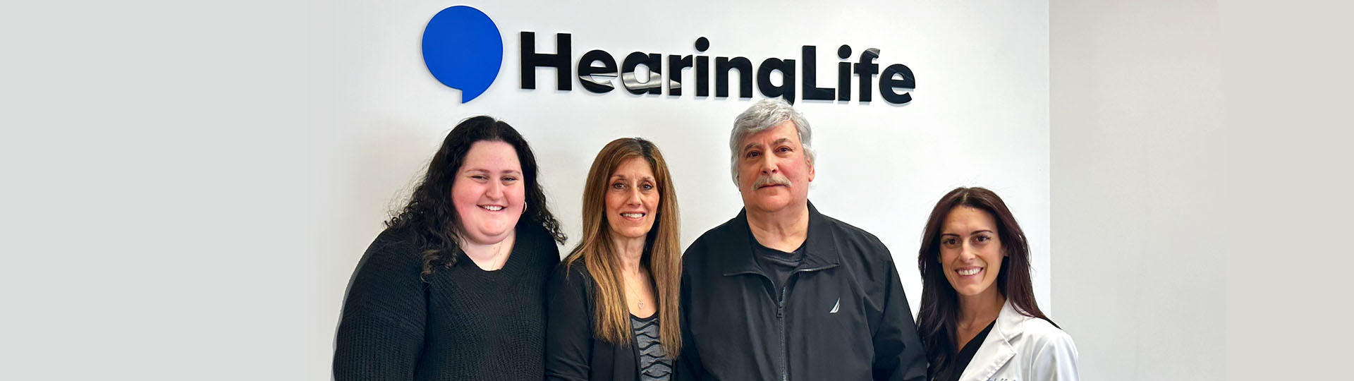 HearingLife team members posing together in front of the HearingLife logo.