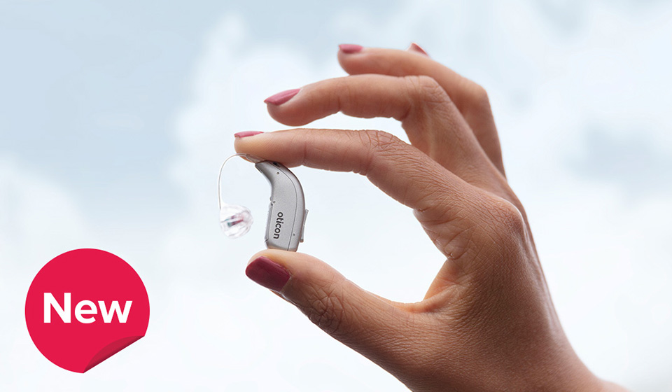 A hand holds a gray hearing aid labeled 
