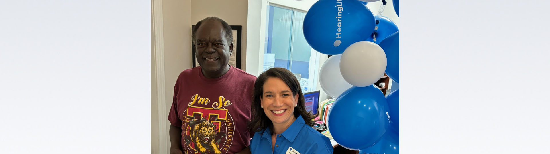 Readie receiving complimentary hearing aids from HearingLife, standing next to a smiling staff member