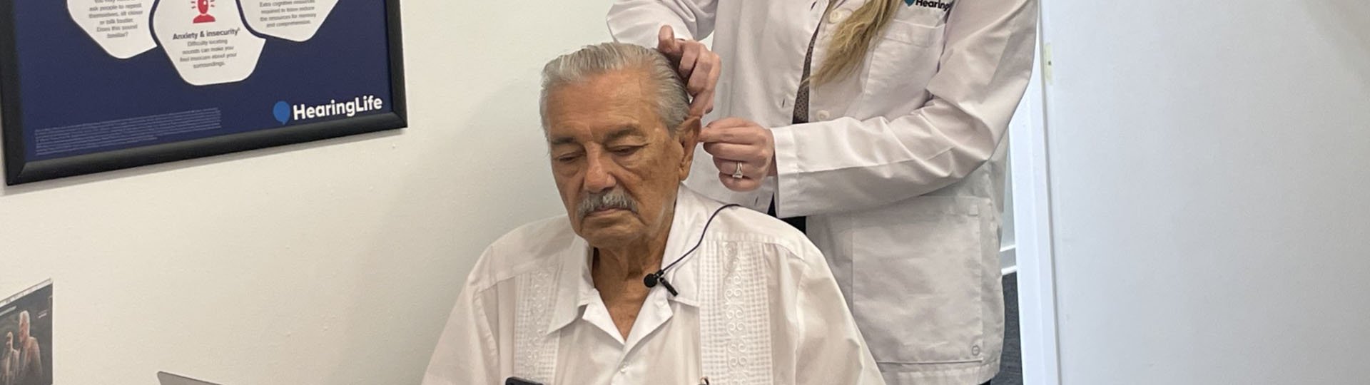 Hearing specialist fitting a hearing aid for an older adult at a HearingLife clinic.