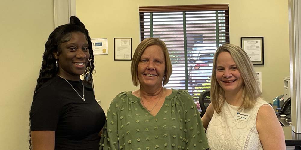 Professional hearing care team standing in an office with certificates displayed on the wall.