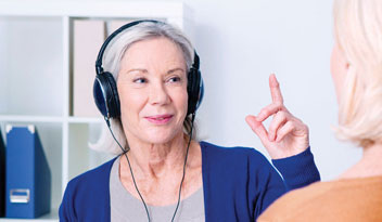 Senior woman taking a hearing assessment with headphones while interacting with a clinician in a professional clinic.