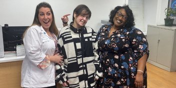 Dawn Gerber standing with a hearing instrument specialist and a patient care coordinator in a hearing clinic setting.