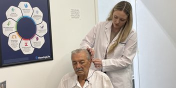 Hearing care specialist fitting a hearing aid on an older adult in a clinic setting.