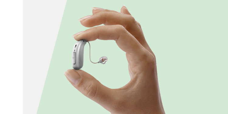 Hand holding a sleek, modern hearing aid between thumb and index finger; minimalistic light green background.