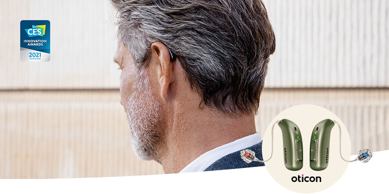 A person with short, graying hair wears a discreet Oticon hearing aid behind their ear. The award-winning Oticon hearing aids are highlighted, showcasing their CES Innovation Awards 2021 badge. The beige backdrop enhances the elegant, advanced hearing technology.