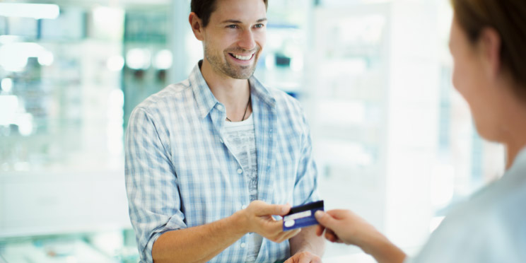 Smiling man in a pharmacy exchanging a credit card with a cashier.