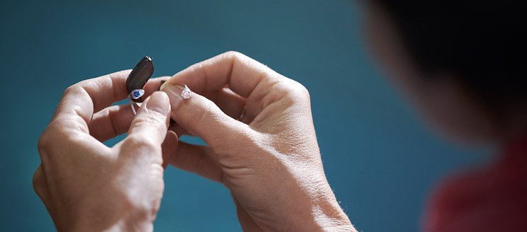 Hands replacing a battery in a hearing aid.