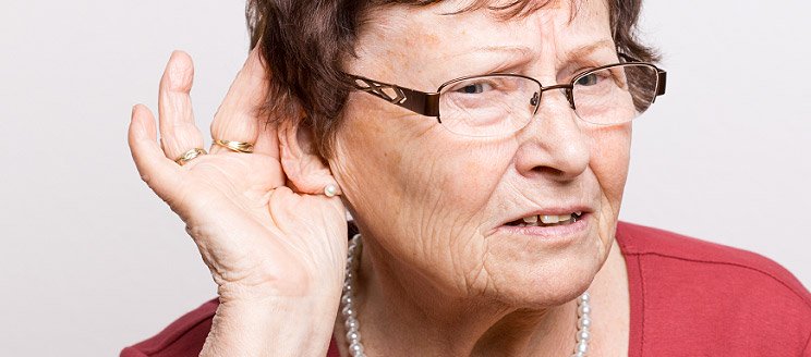 Elderly woman cupping hand near ear to hear more clearly.