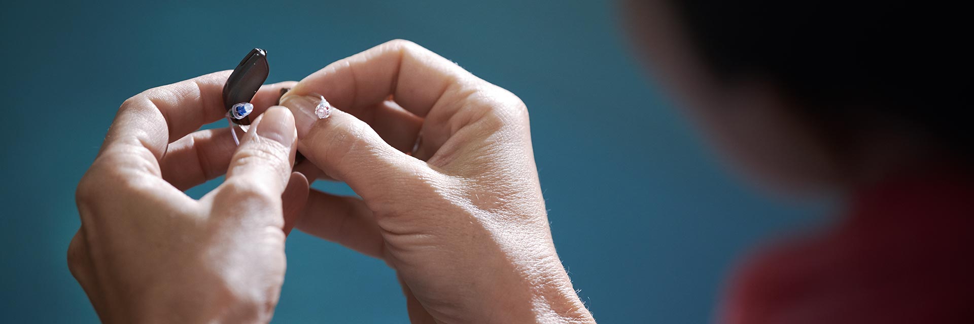 Hands replacing a hearing aid battery on a blue background.