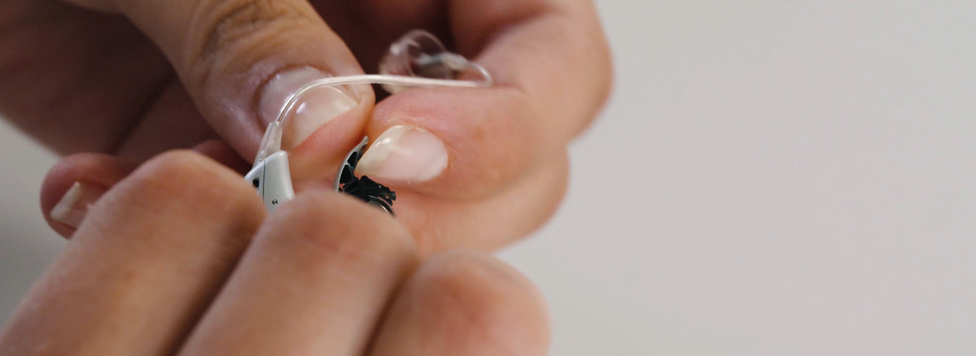Hands gently adjusting a sleek modern hearing aid with precision.