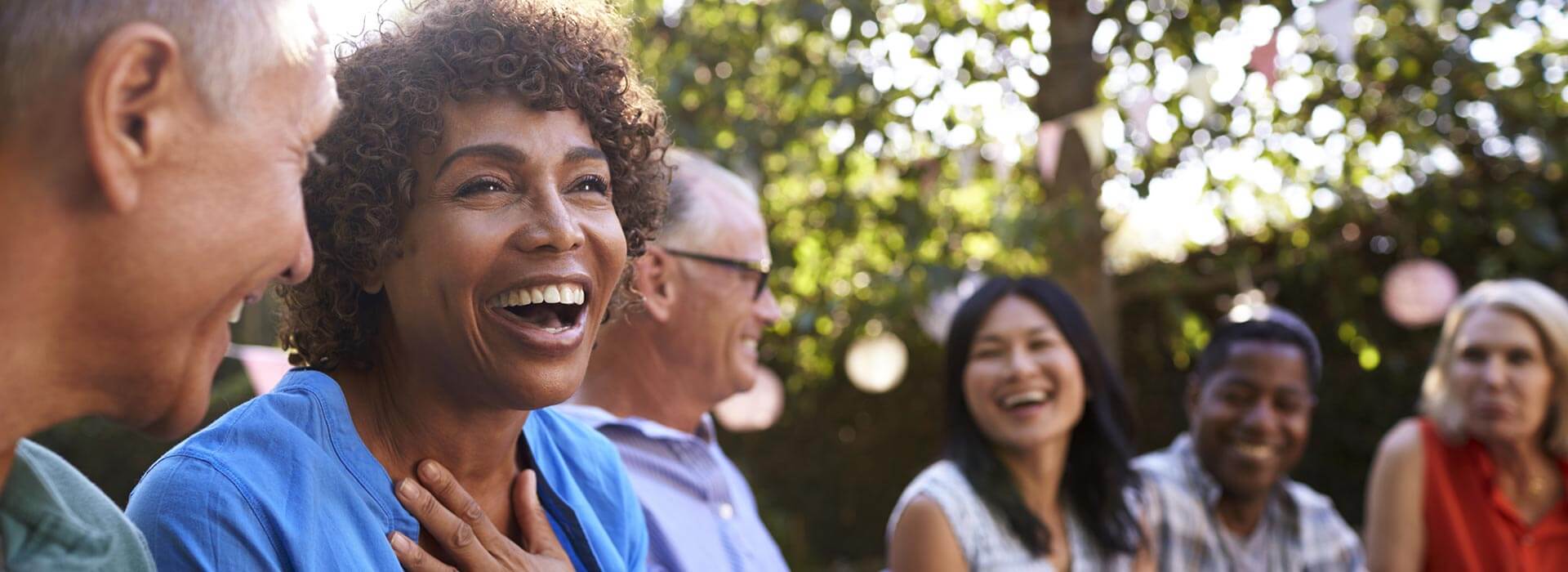 People enjoying laughter outdoors on a sunny day, surrounded by lush trees and decorative hanging ornaments.